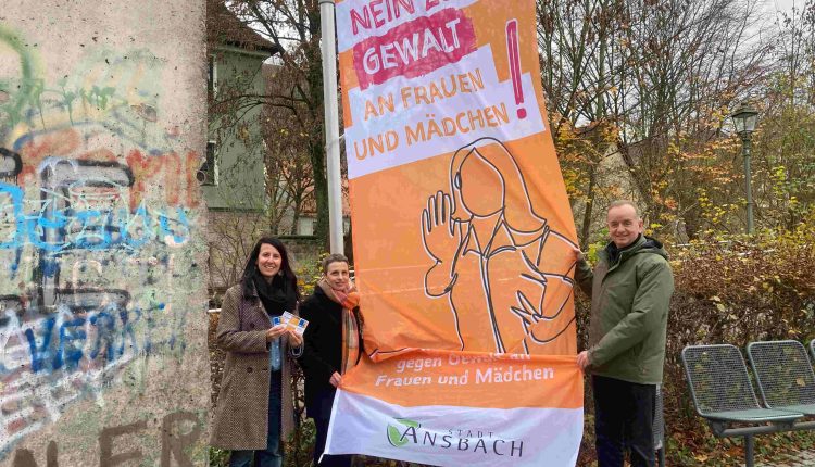 Tanja Peipp, Lisa-Marie Buntebarth und Thomas Deffner neben der Fahne zum „Internationalen Tag gegen Gewalt an Frauen und Mädchen“